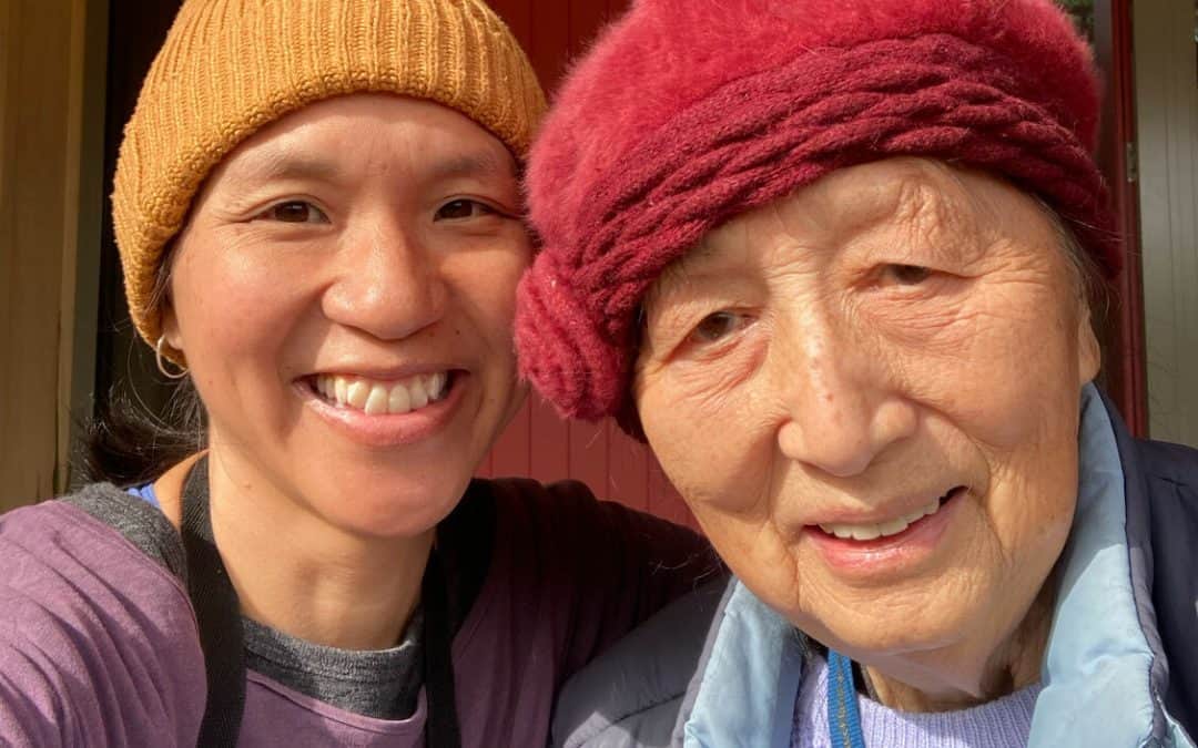 face portrait of two asian ladies with woolen hats, younger on left with sand coloured hat, older one with red coloured hat on right