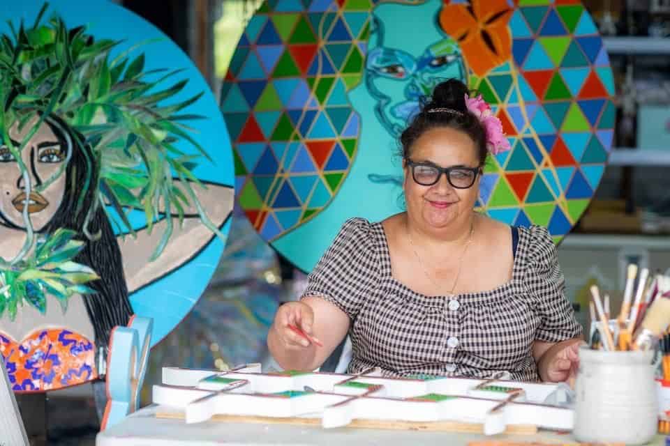 Woman with thick balck rimmed gallses doing creative work in front of colourful background