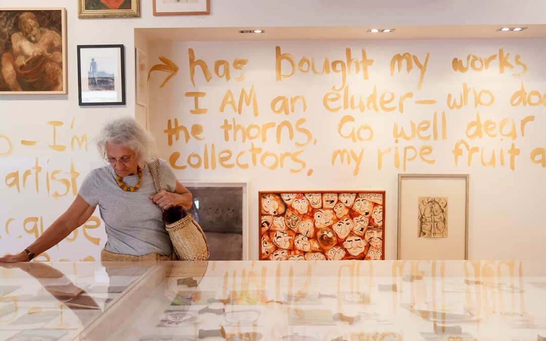 exhibition space with writing on wall and woman with grey hair looking at display cabinet