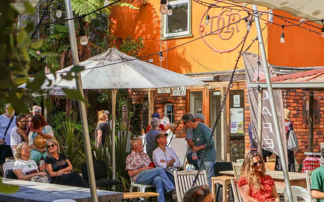 poeple sitting in summery yard under sun umbrellas with organge coloured house in background