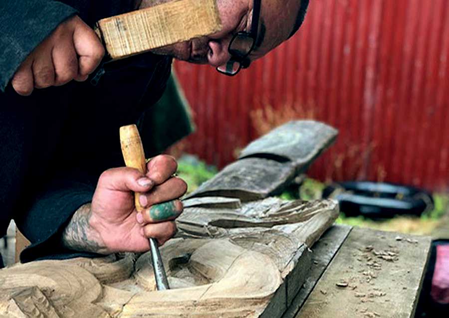 man with chisel and mallet carving a maori carving