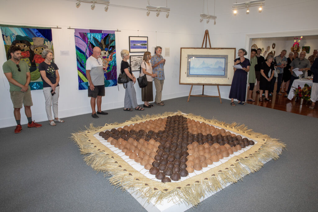 exhibition space with a large ground sculpture showing a cross made from natural fibres and materials