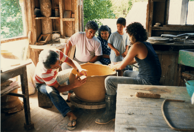 several potters sitting around a clay vessel they are building
