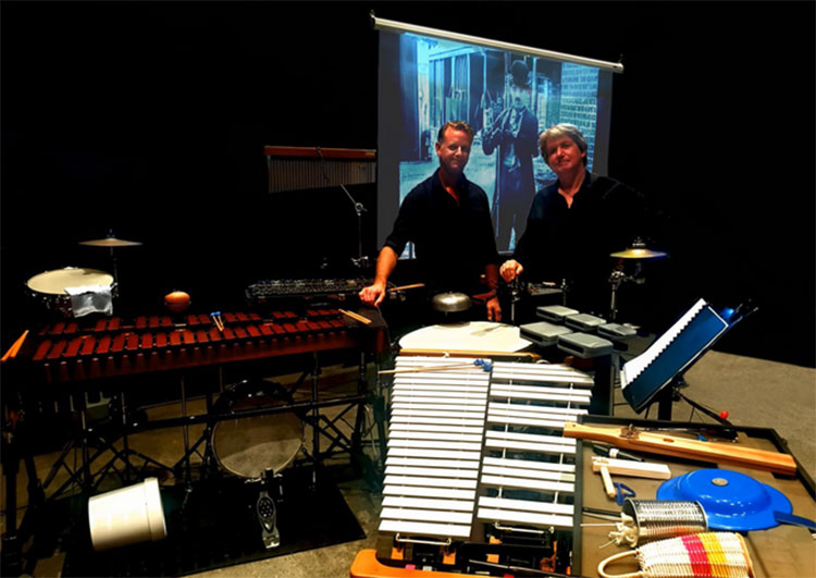 two men with lots of musical instruments and a movie screen in the background