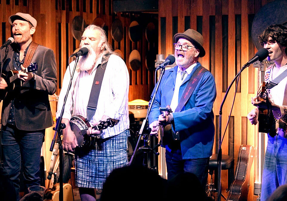 four older mae musicians on stage singing and playing isntruments