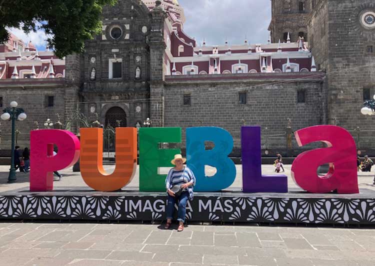 woamn sitting on edge of a street scuplture with the word PUEBLa in Mexcain city