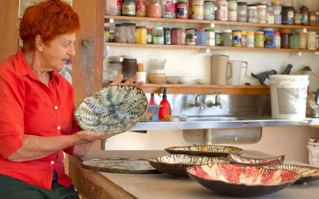 woman in orange shirt holding a ceramic plate in her studio