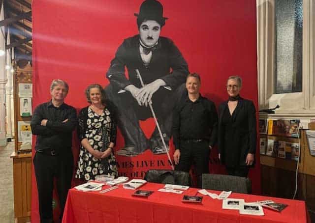 several people in balck clothees in fron tof a red banner with a black and white picture of Charlie Cahplin